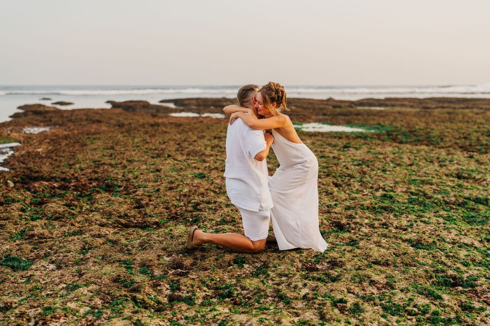 A couple shares an intimate moment on a rocky beach during sunset.