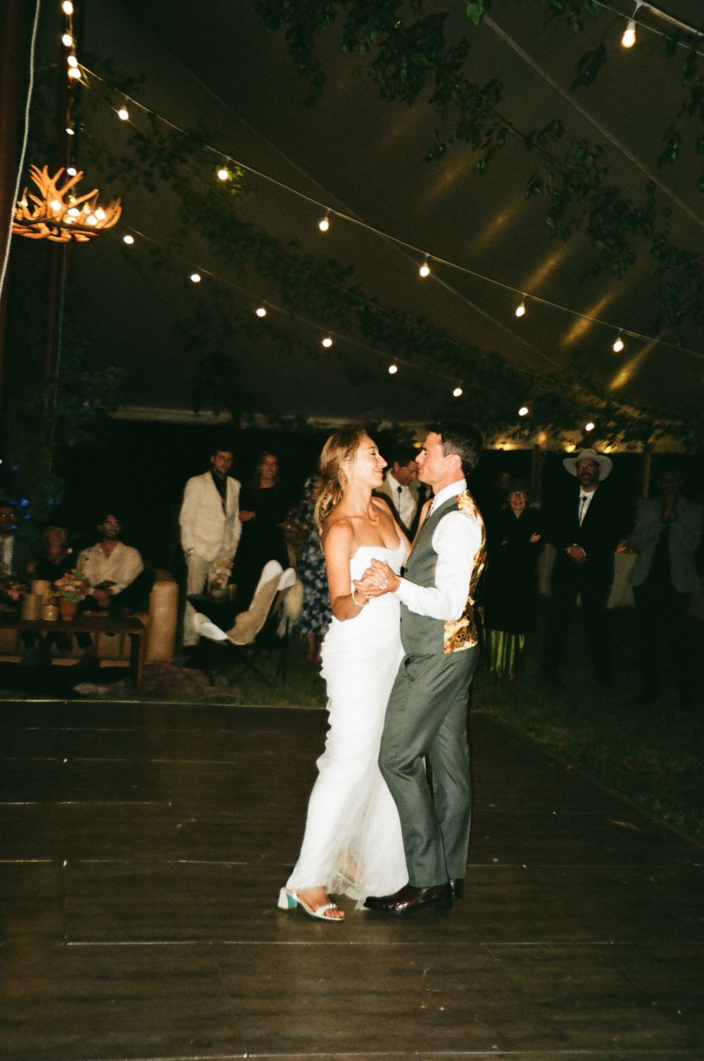 Couple dancing under string lights at outdoor wedding reception.
