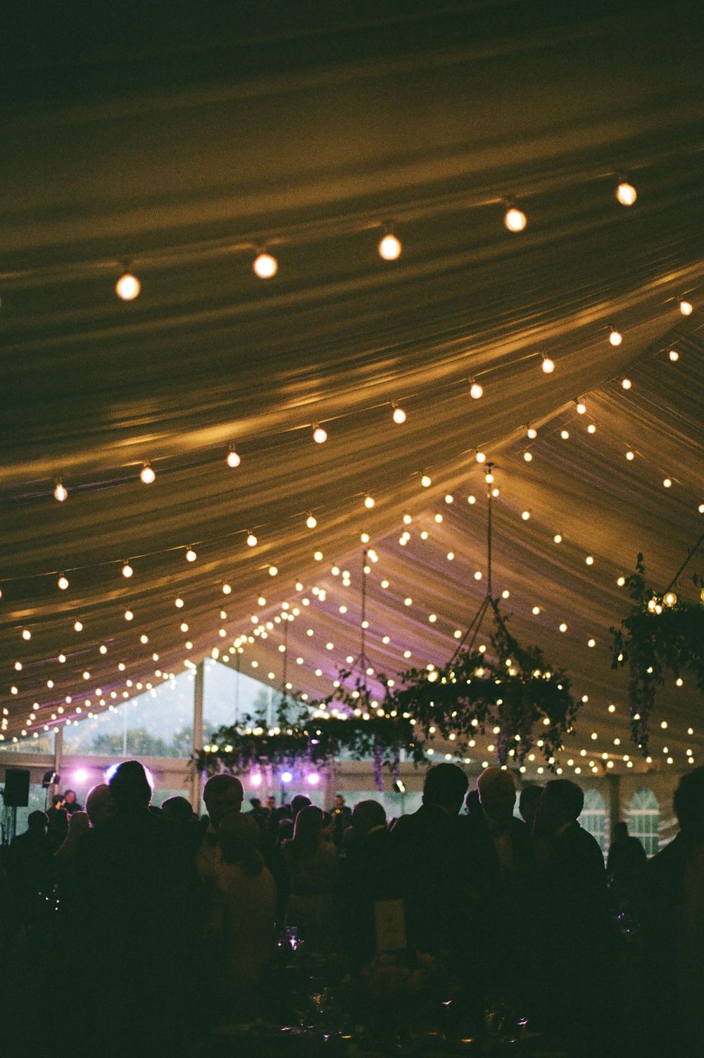 Wedding reception tent illuminated with string lights creating a magical evening ambiance.