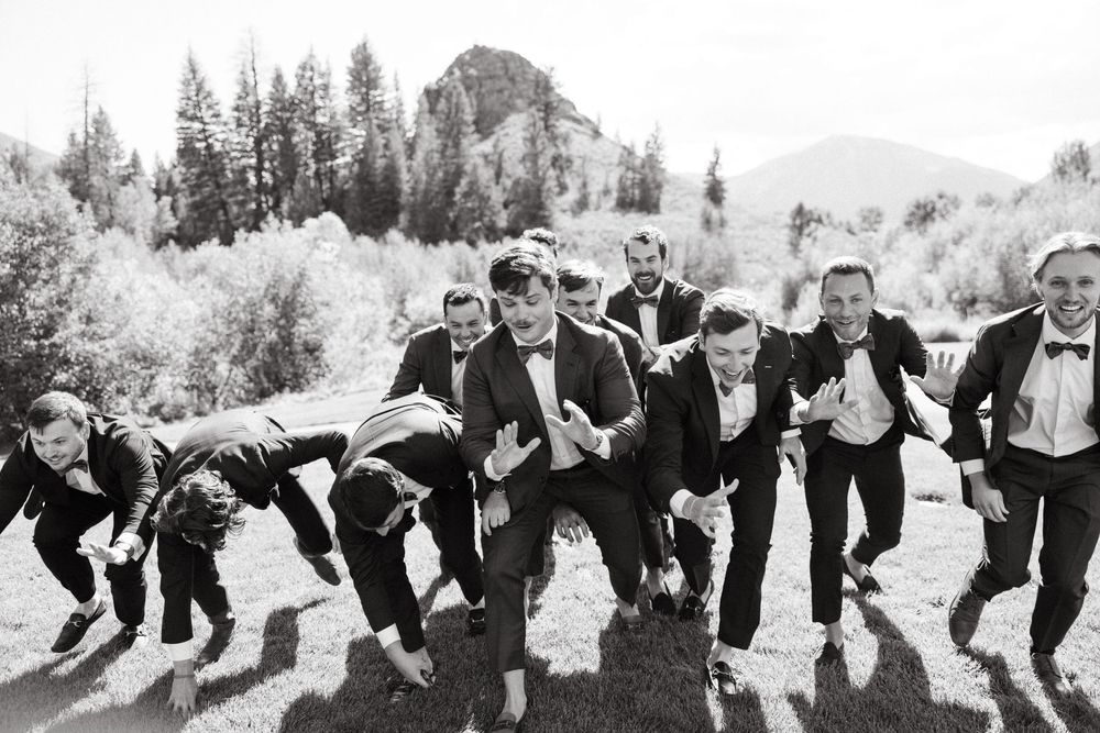 Wedding party members line up and lean to one side in a playful group pose against an outdoor backdrop.
