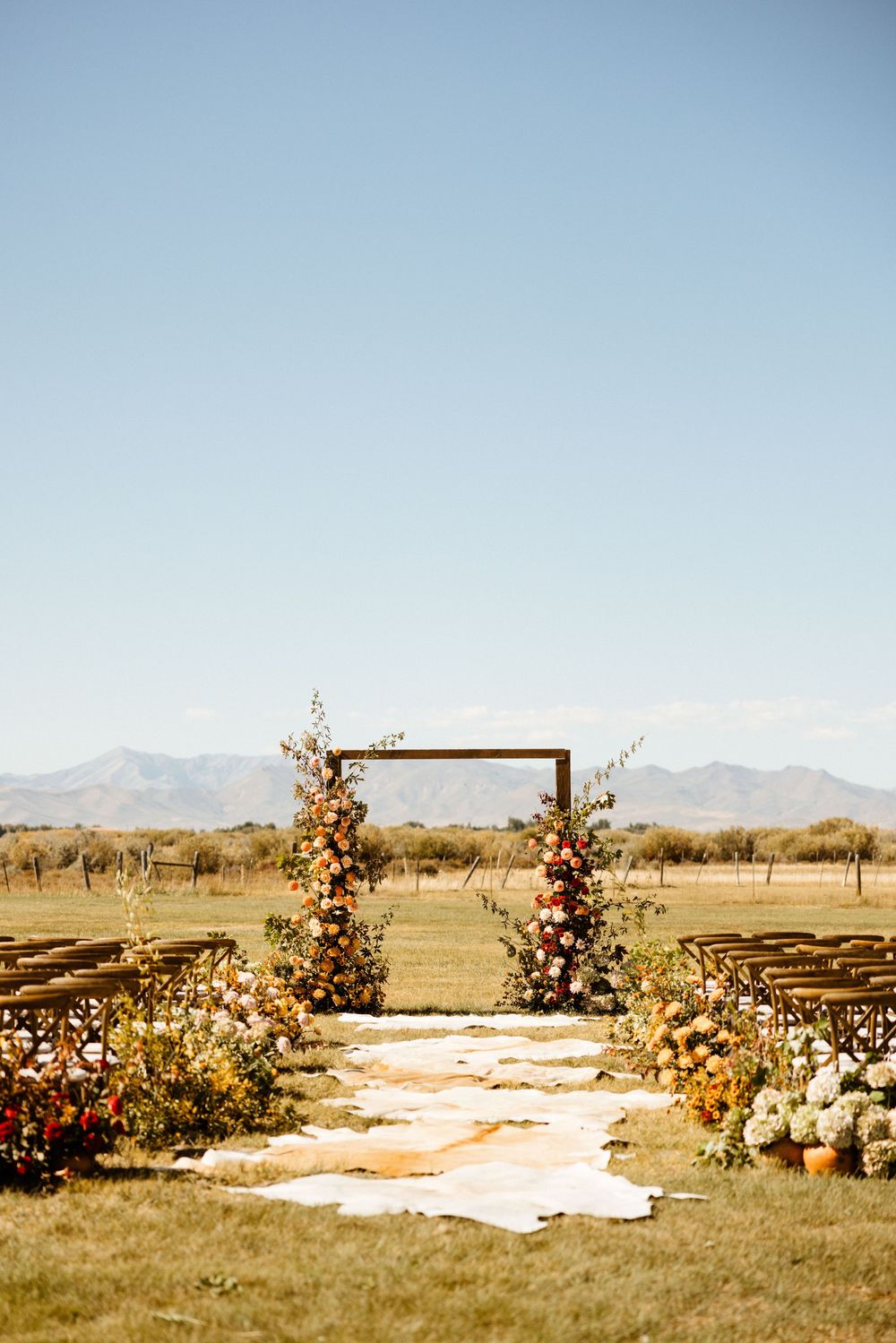 Outdoor wedding ceremony setup with floral arch and white aisle runner in a desert landscape.