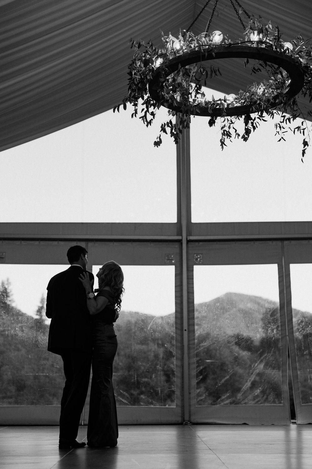 Silhouetted figures dance in an elegant venue with mountain views through large windows.