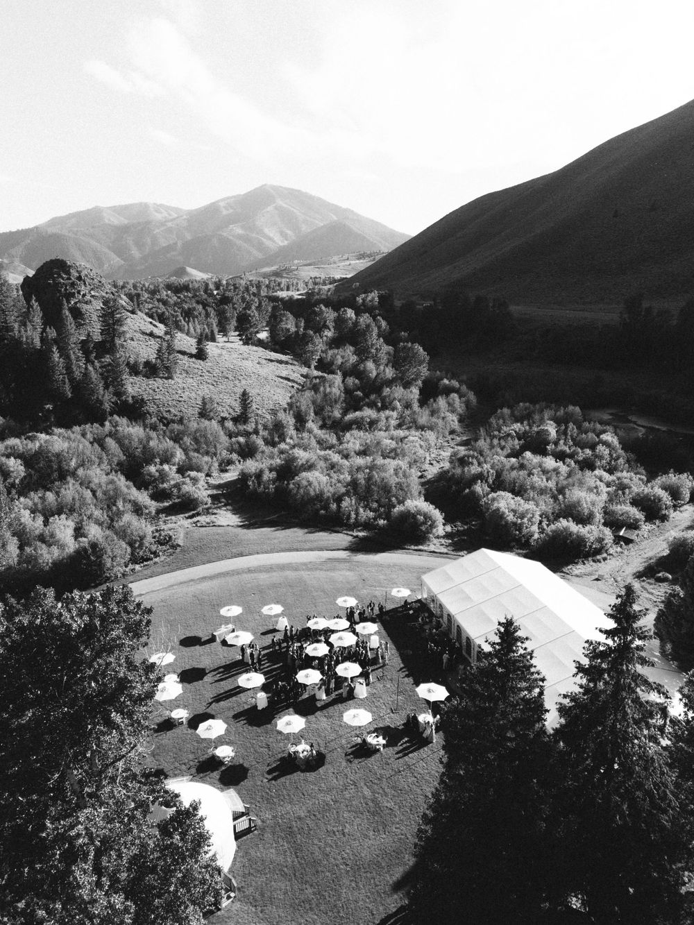 Aerial black and white view of mountain venue with white reception tents and scenic landscape.