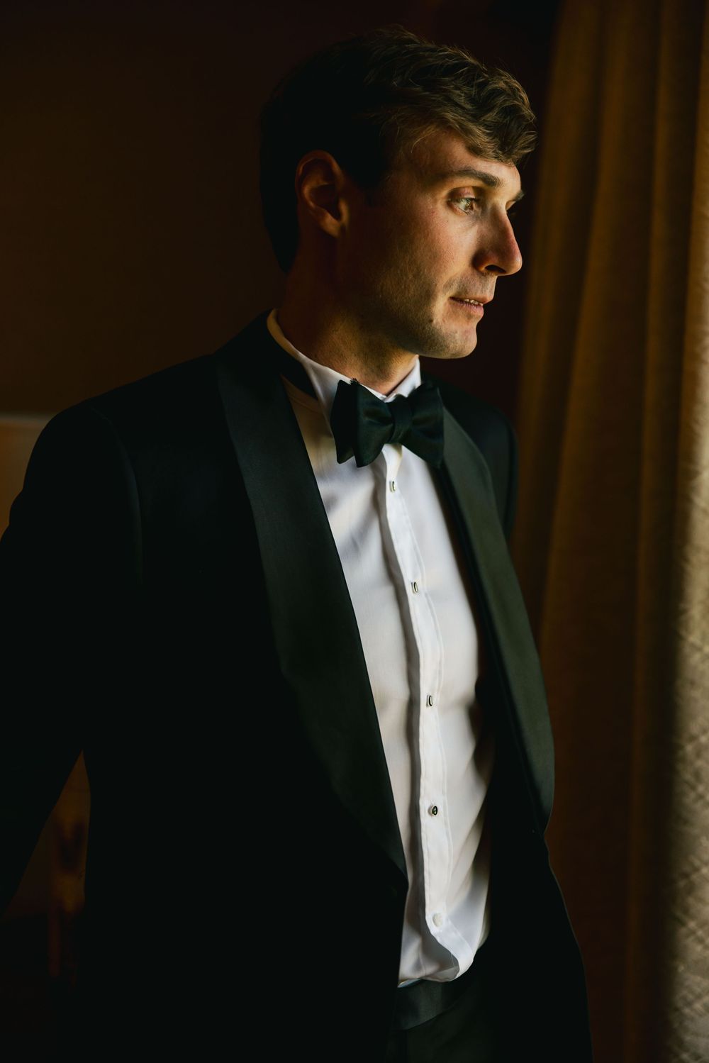 Dramatic side profile shots of groom in tuxedo with moody lighting and dark background.