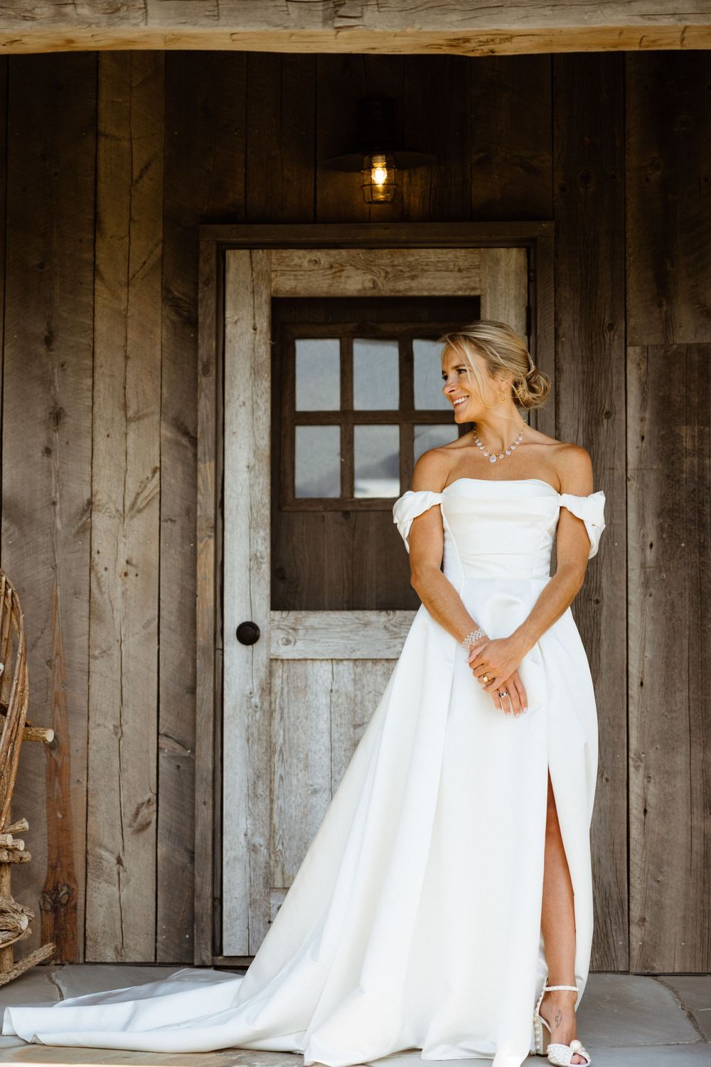 Bride in elegant white wedding dress posing in rustic wooden barn setting.