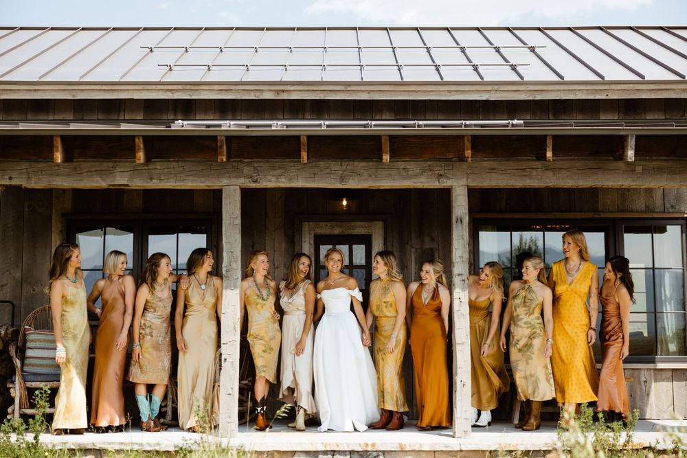 Wedding party in yellow and white dresses lined up under rustic porch roof.