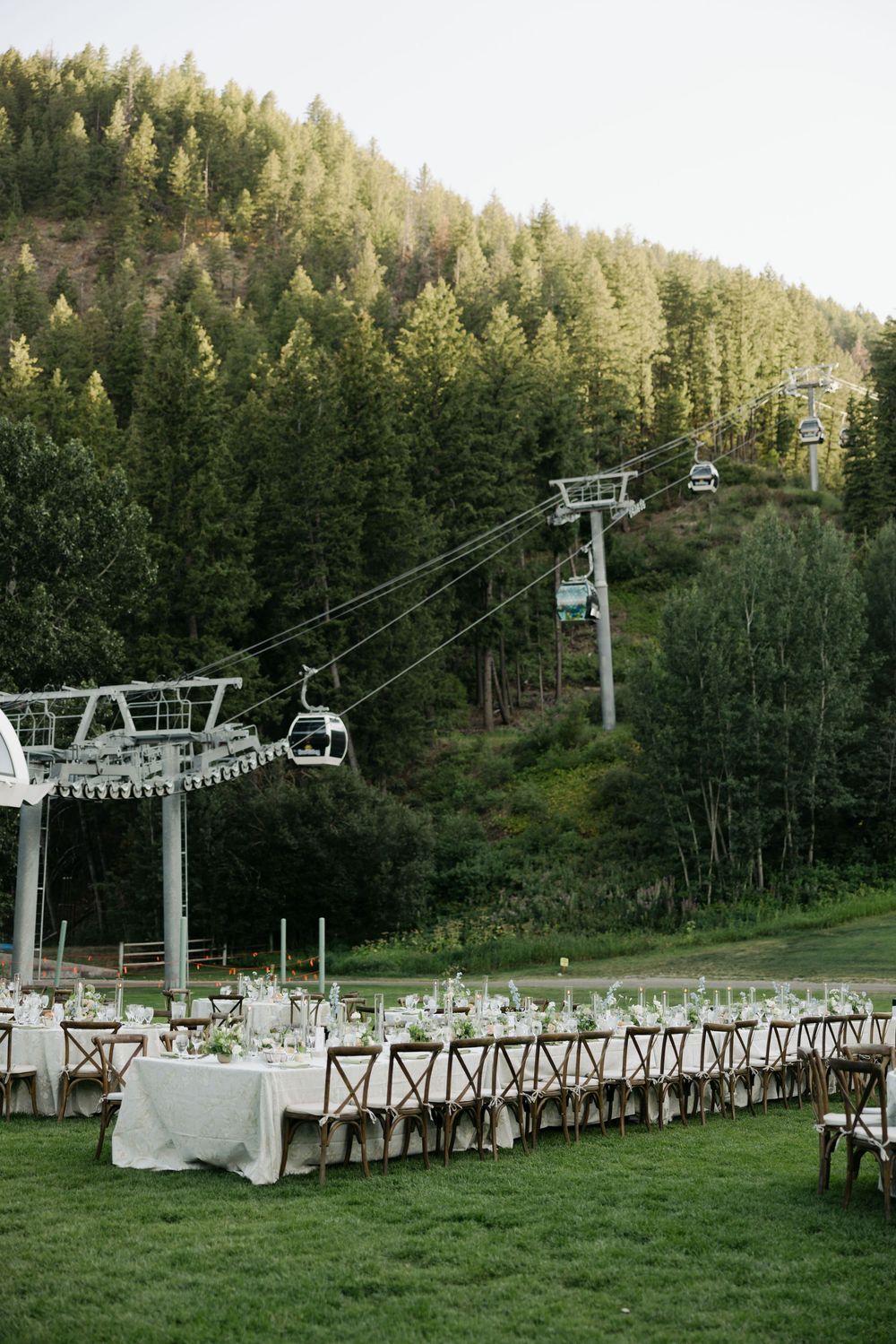 Mountain wedding reception setup with long tables beneath ski lift chairs.