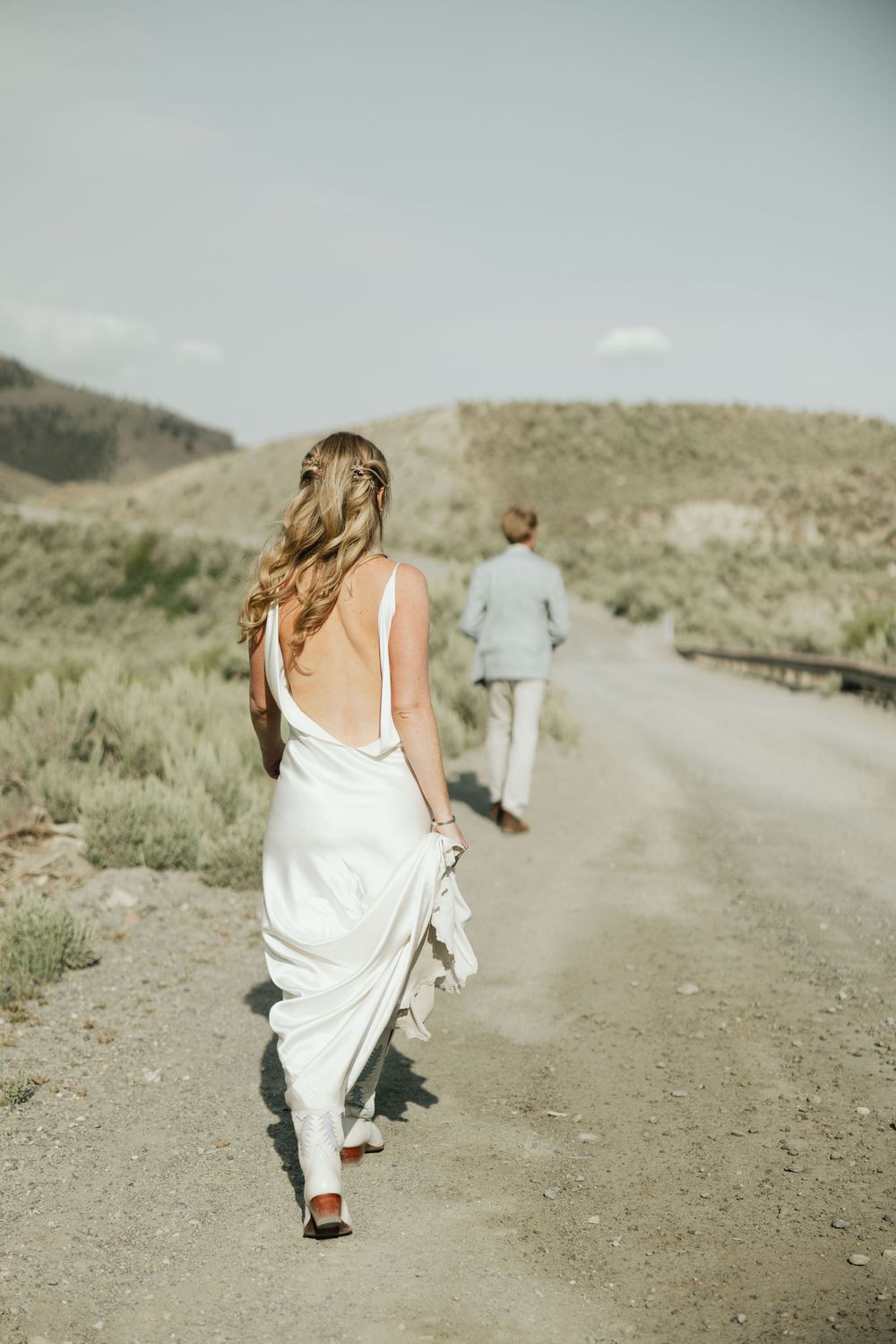 Couple walks along a dusty mountain road in wedding attire.