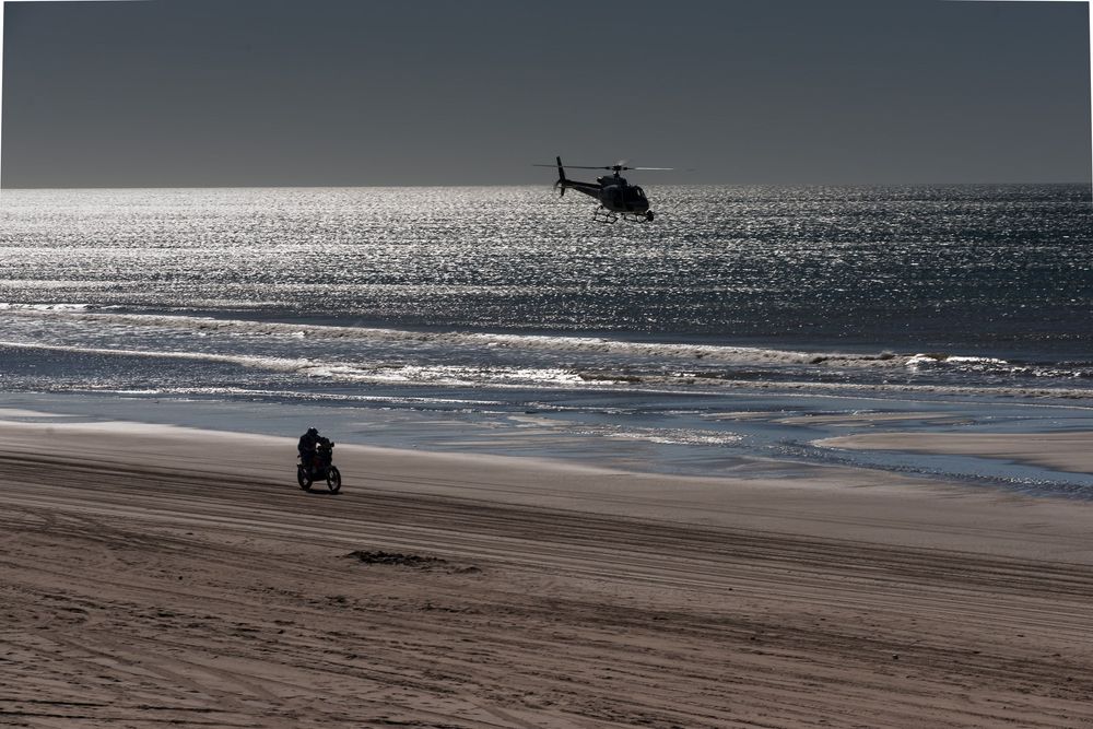 Panoramic view of a deserted beach shoreline with silhouetted figures and crashing waves at dusk.
