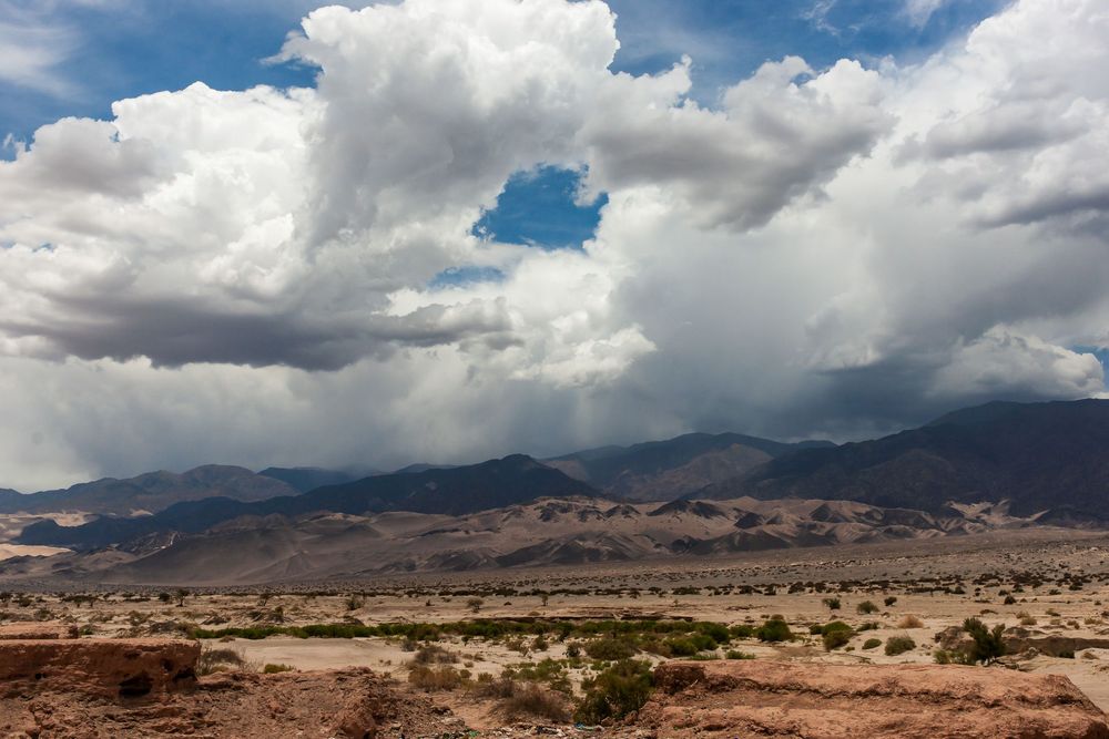 Dramatic storm clouds roll over a vast desert landscape with mountains visible in the background.
