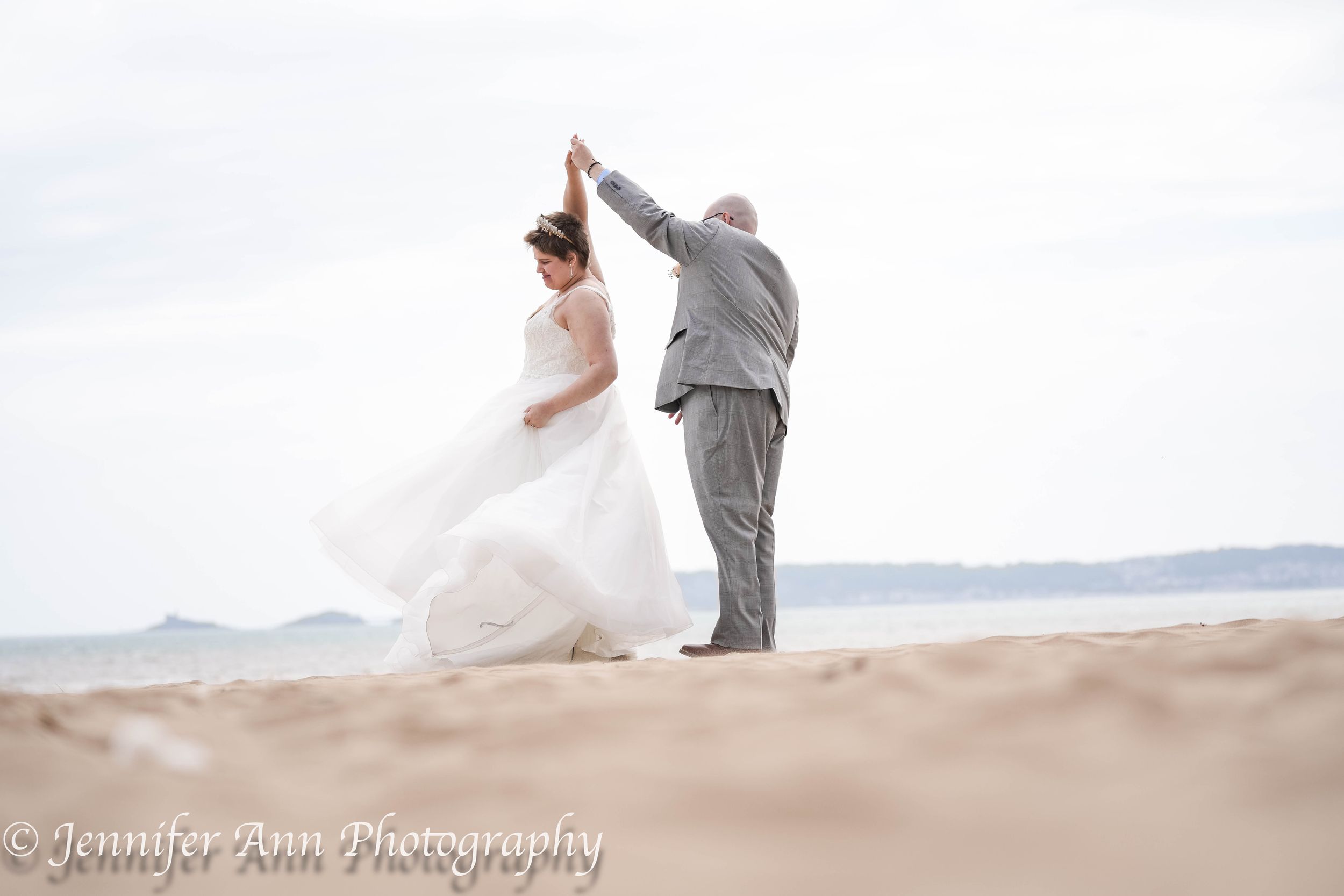 Couple walking and dancing together on sandy beach dunes at sunset creating romantic silhouettes.