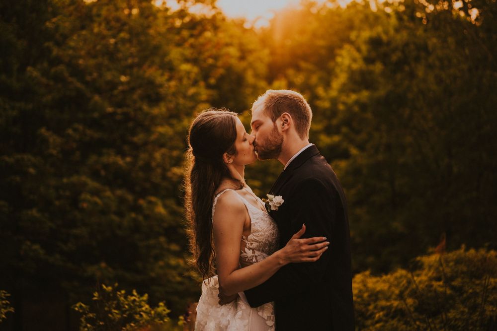Couple sharing a romantic kiss at golden hour surrounded by trees.