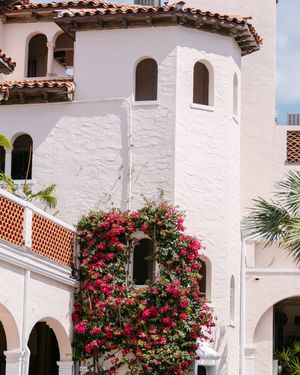 Spanish colonial architecture with white stucco walls, terracotta roof tiles, and vibrant pink bougainvillea flowers climbing the arches.