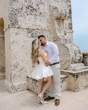 Romantic couple sharing intimate moments against a stone wall in an elegant setting.
