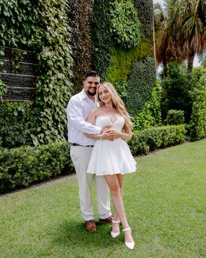 Couple in white outfits shares playful moments in a lush garden setting.