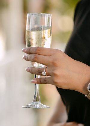 A hand holding a champagne flute displays an elegant engagement ring with bubbling champagne in the glass.
