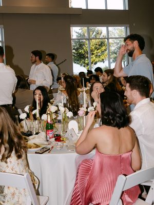 Guests in formal attire seated at decorated tables during an elegant wedding reception in a bright venue.