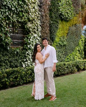 A couple poses against a wall covered in lush green ivy and climbing plants.