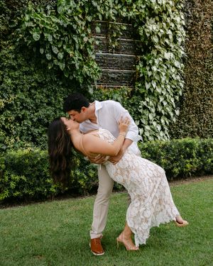 Romantic couple in formal wear dances and dips in lush garden setting.