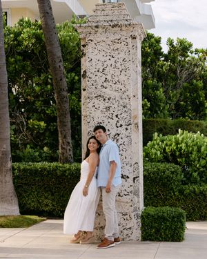 Couple poses together against stone columns in tropical garden setting.