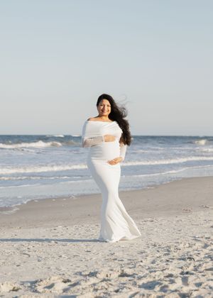 A person in a flowing white dress dances gracefully along a sandy beach with ocean waves in the background.