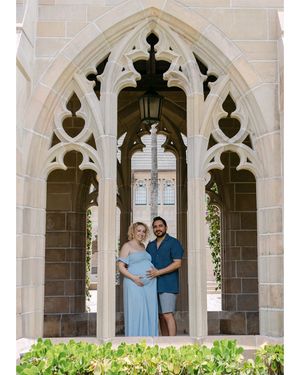 Couple poses in elegant Gothic archways surrounded by lush greenery at a historic venue.