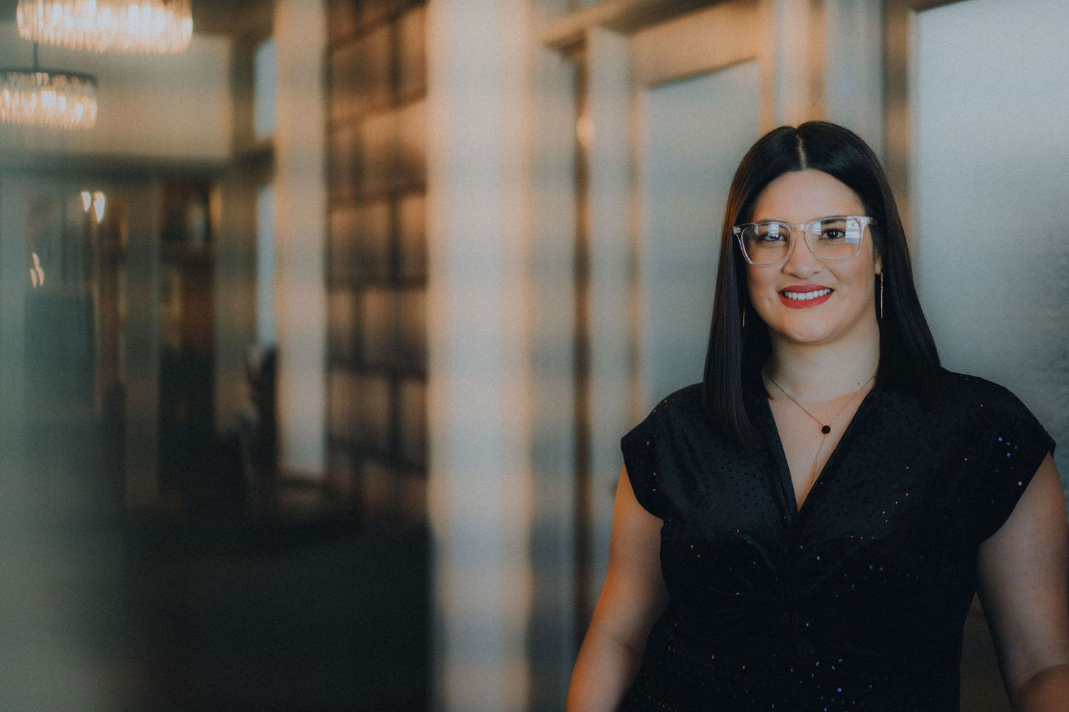Professional figure in a black top stands in an office hallway with soft lighting creating a warm atmosphere.
