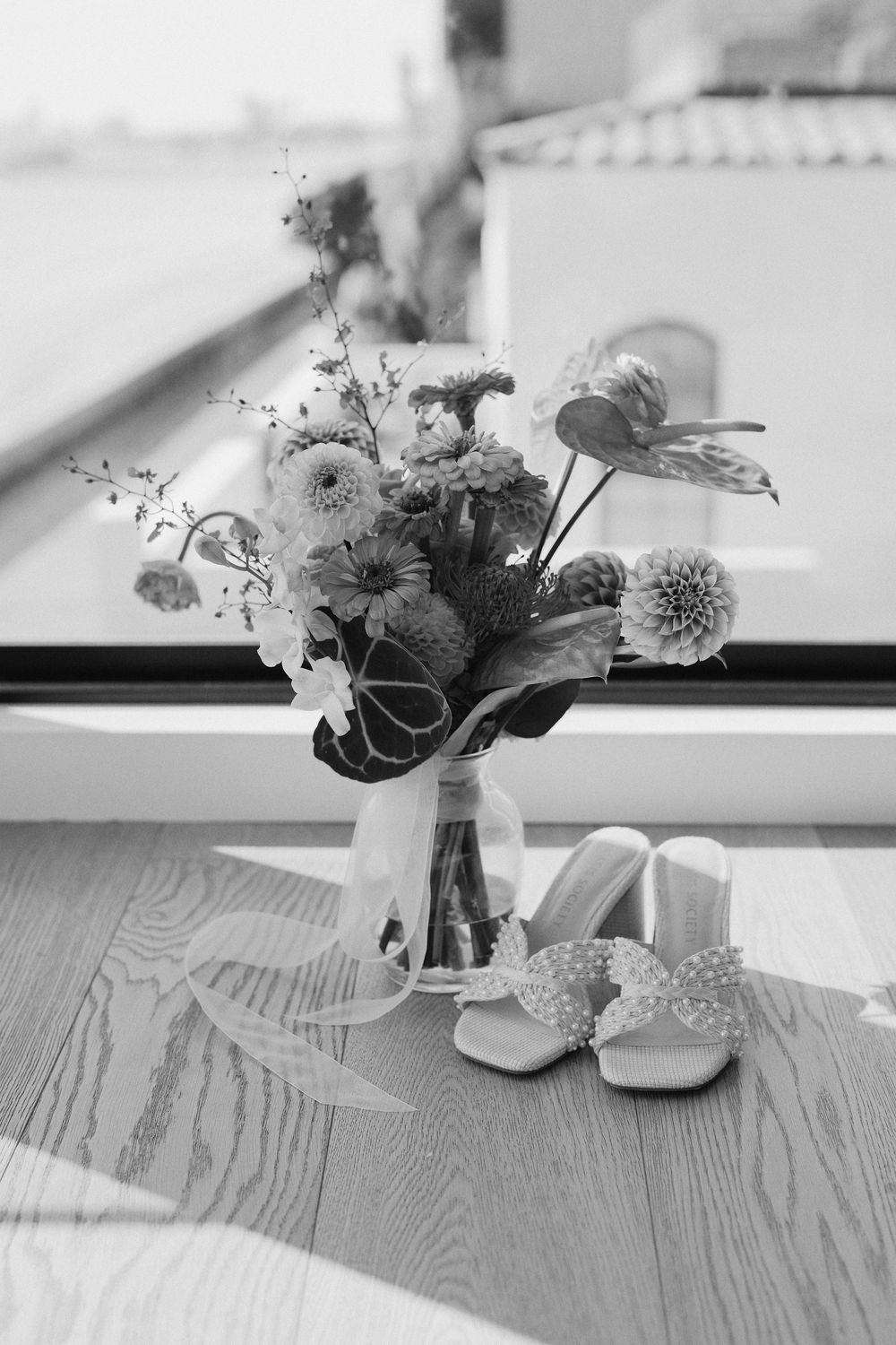 A series of black and white floral arrangements in small vases lined up on a wooden surface near a window.