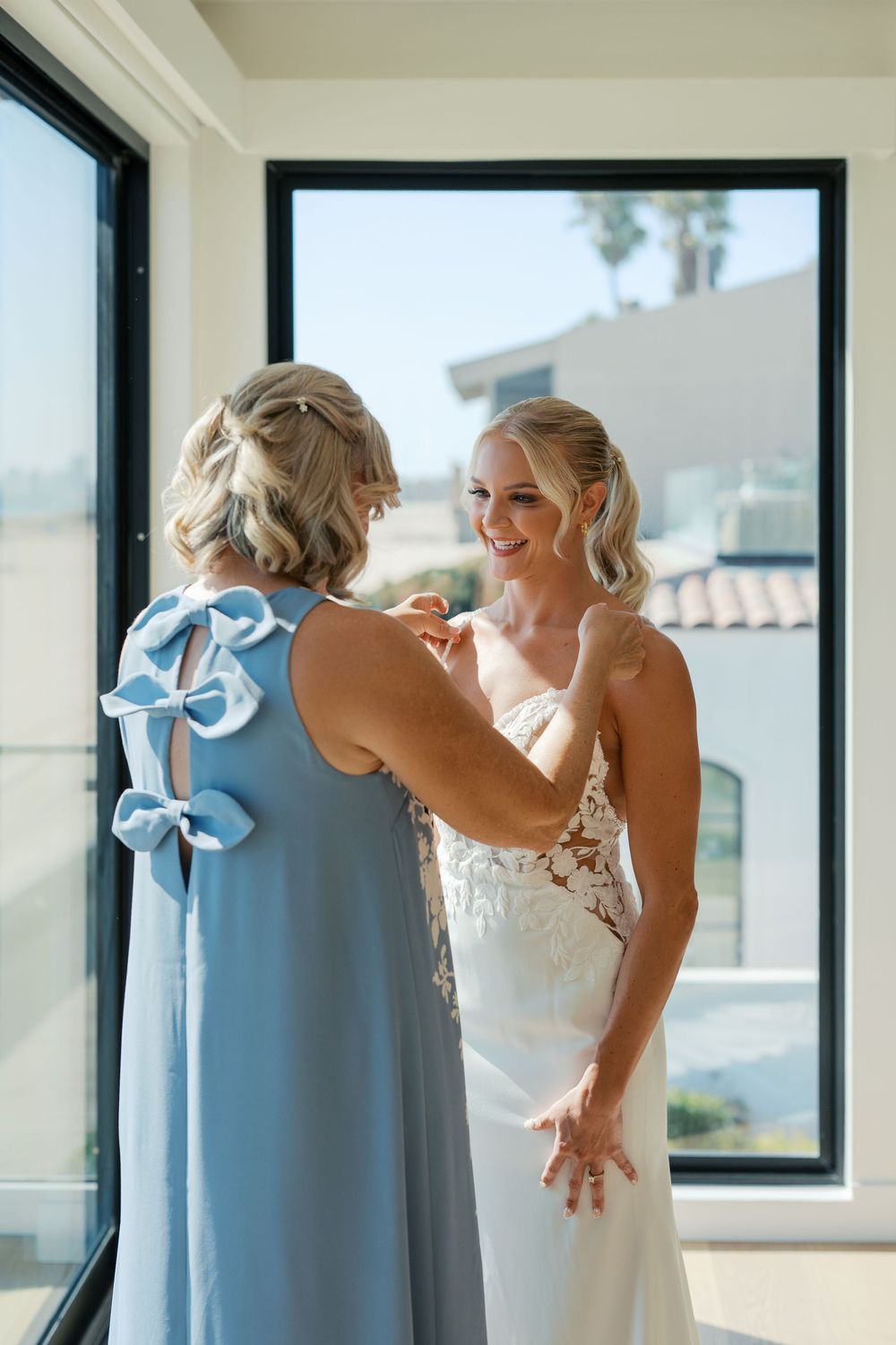 Light blue bridesmaid dresses hanging neatly by a sunny window during wedding preparations.