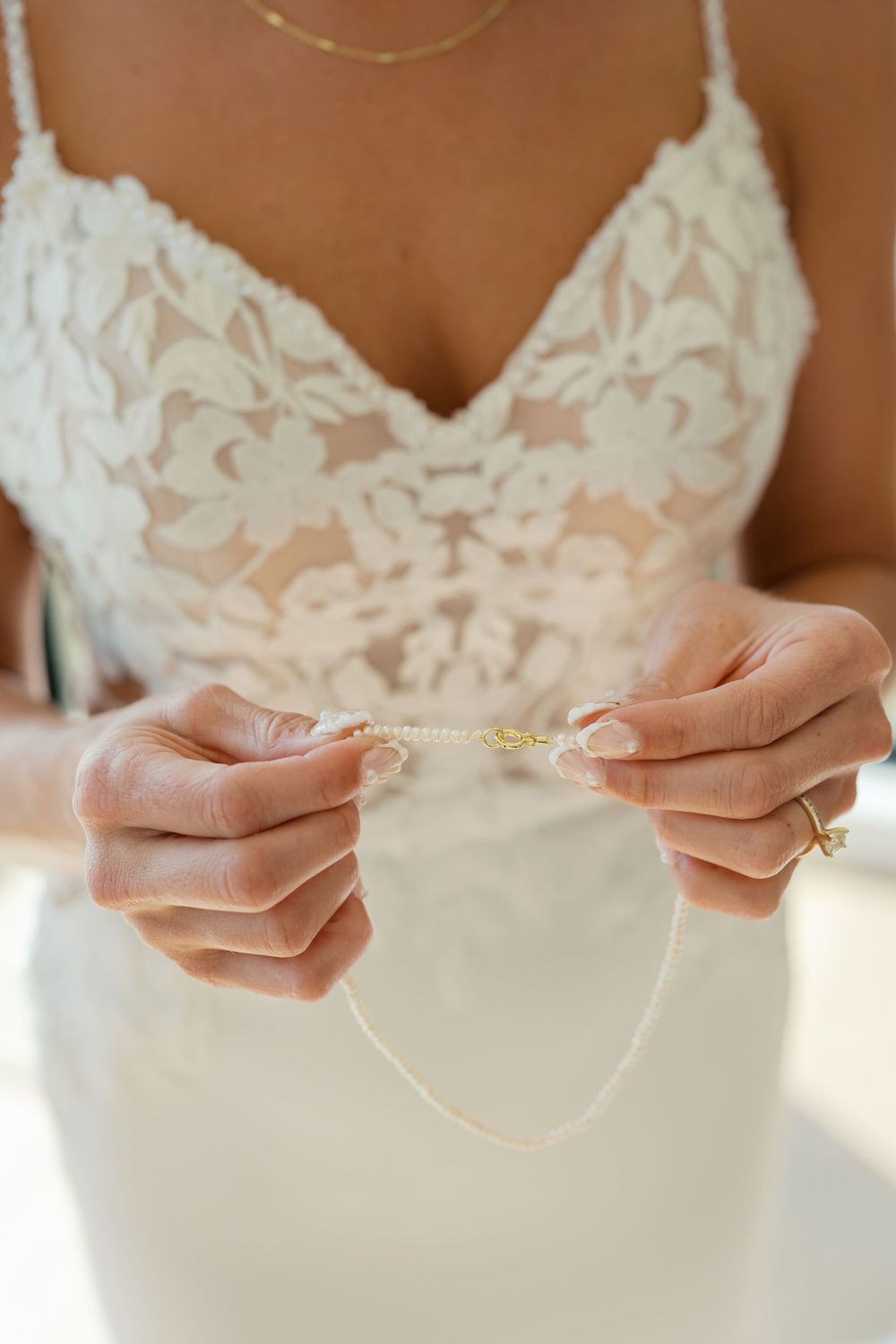 Close-up sequence of hands holding and adjusting a delicate necklace against a white lace bodice.