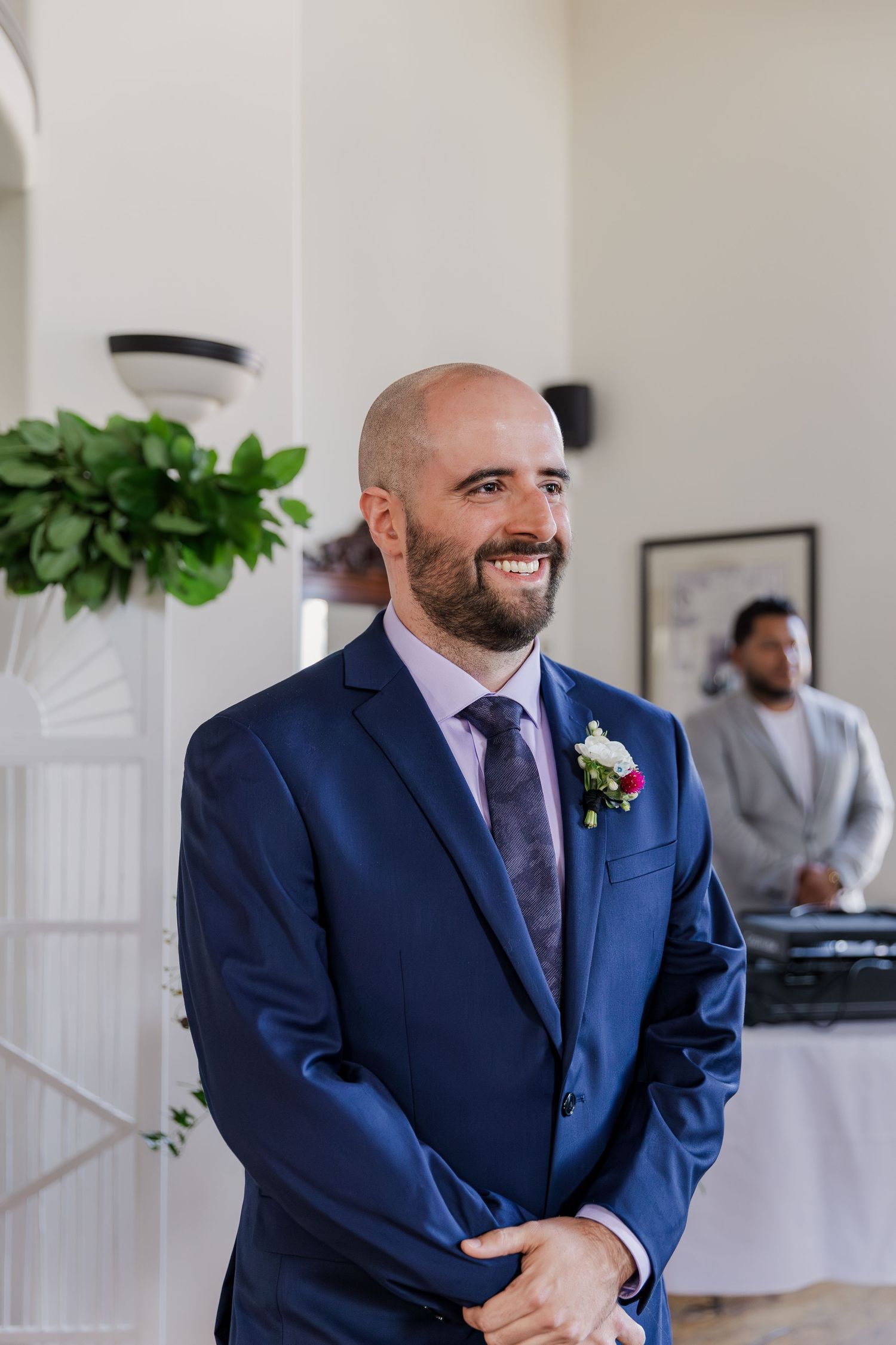 Groom standing at the front of the ceremony smiles when he sees his bride for the first time at Hauser Hall in Kitchener, Ontario.