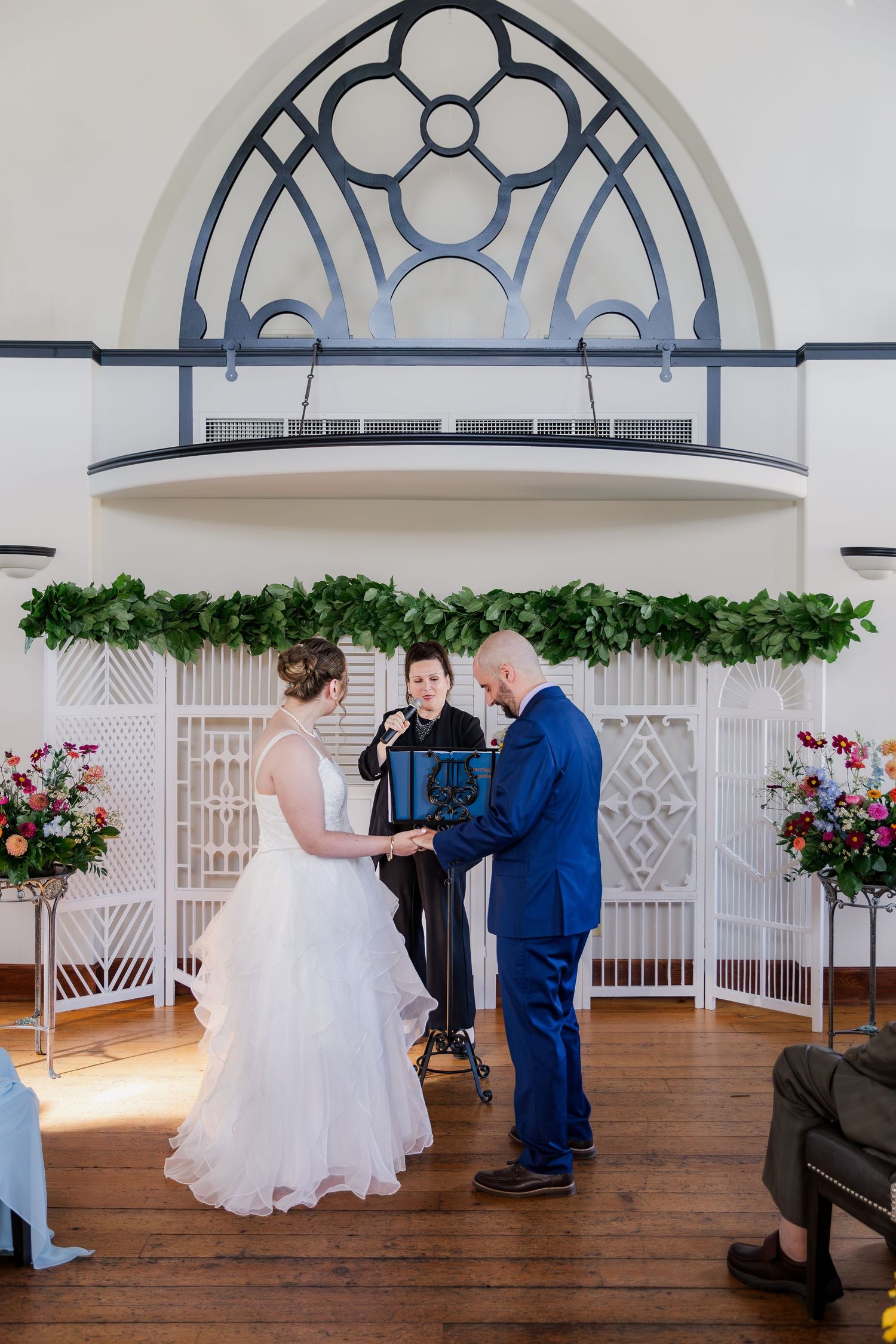 Bride and groom hold hands during their ceremony under ornate arched alcove with greenery and florals at Hauser Hall in Kitchener.