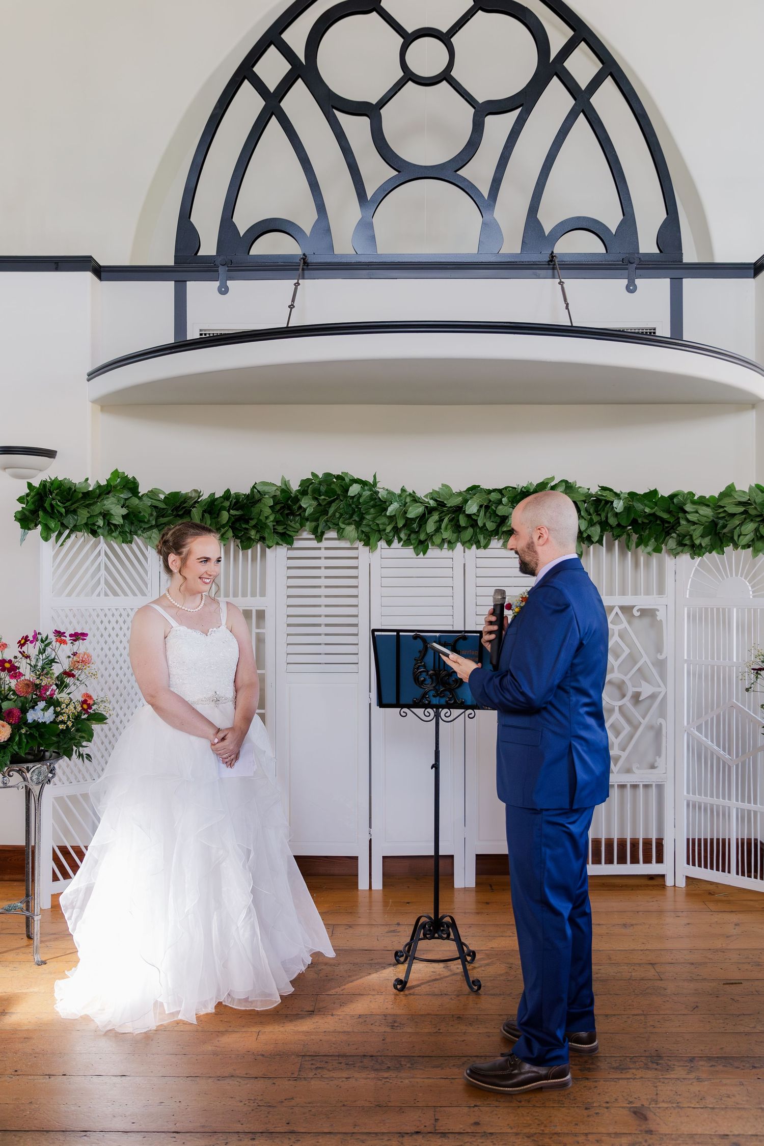 Wedding ceremony with couple standing under ornate white archway with greenery decorations at Hauser Hall in Kitchener, Ontario.
