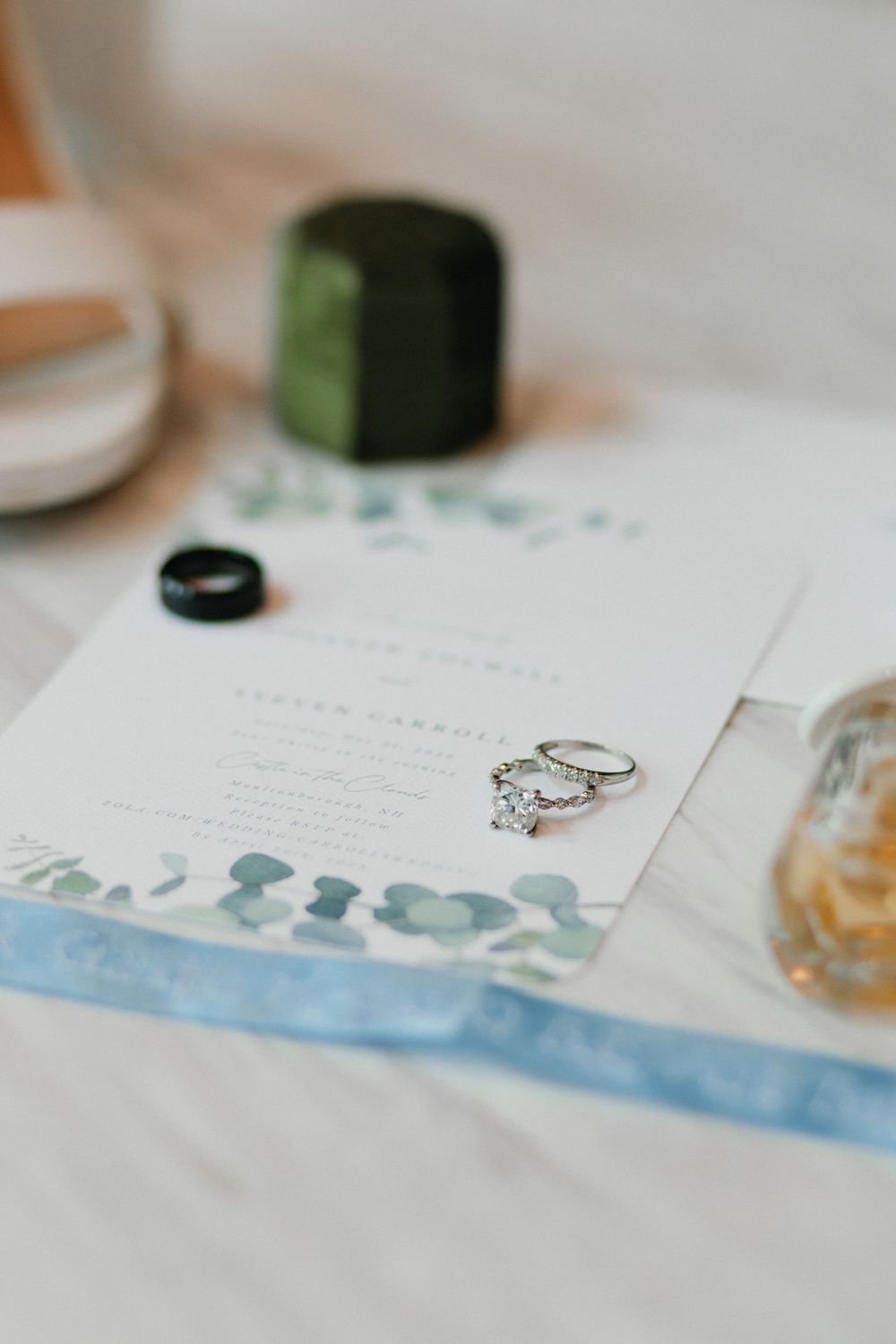 Wedding invitation with watercolor border details and engagement ring on display.