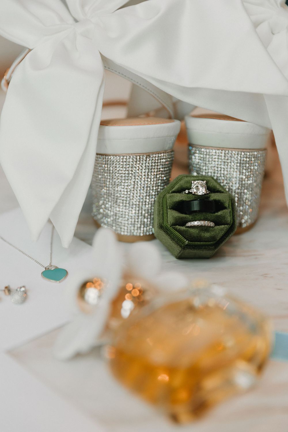 Wedding accessories including sparkly shoes and green velvet ring box arranged artistically.