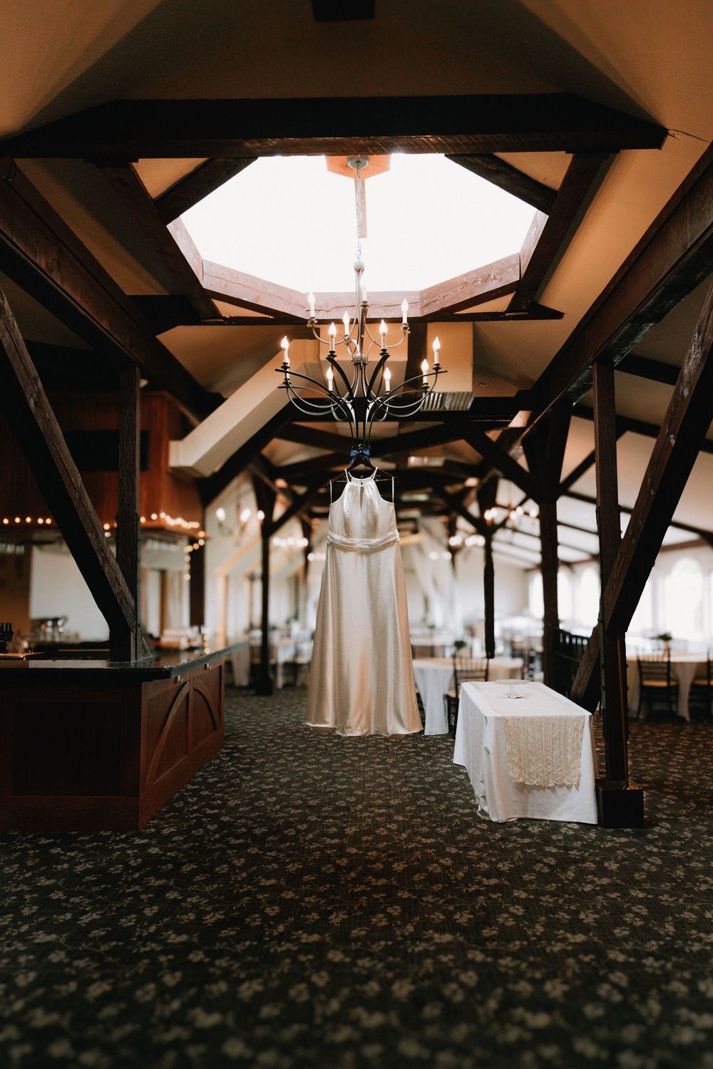 Wedding dress hanging in a rustic venue with exposed wooden beams and chandeliers.
