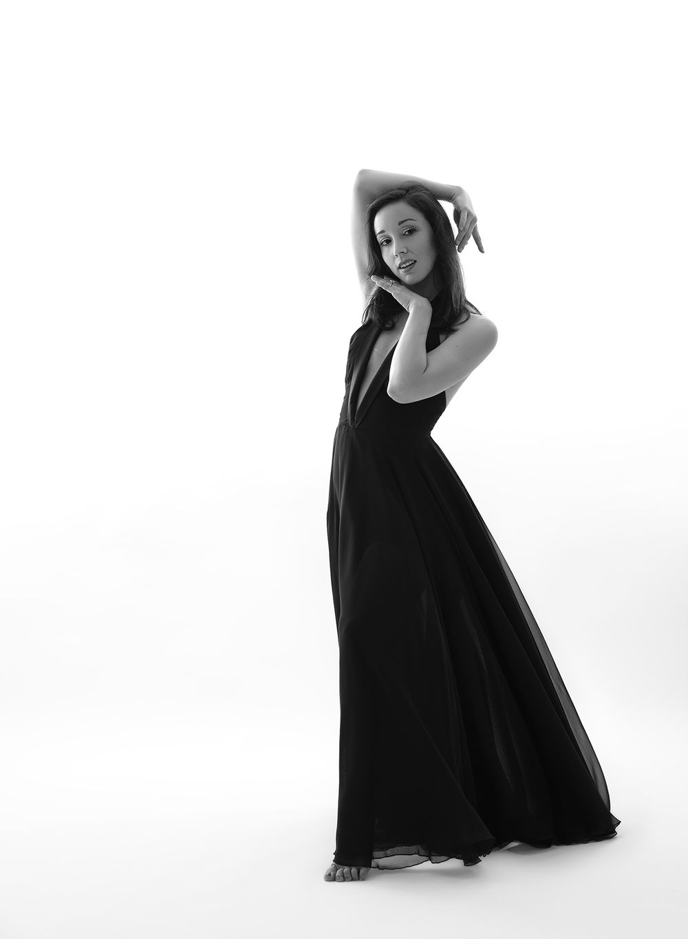 A figure strikes four elegant poses in a flowing black dress against a stark white background, creating dramatic silhouettes.