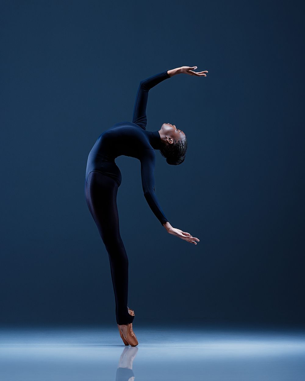A dancer performs a dramatic back bend sequence in silhouette against a dark blue background.