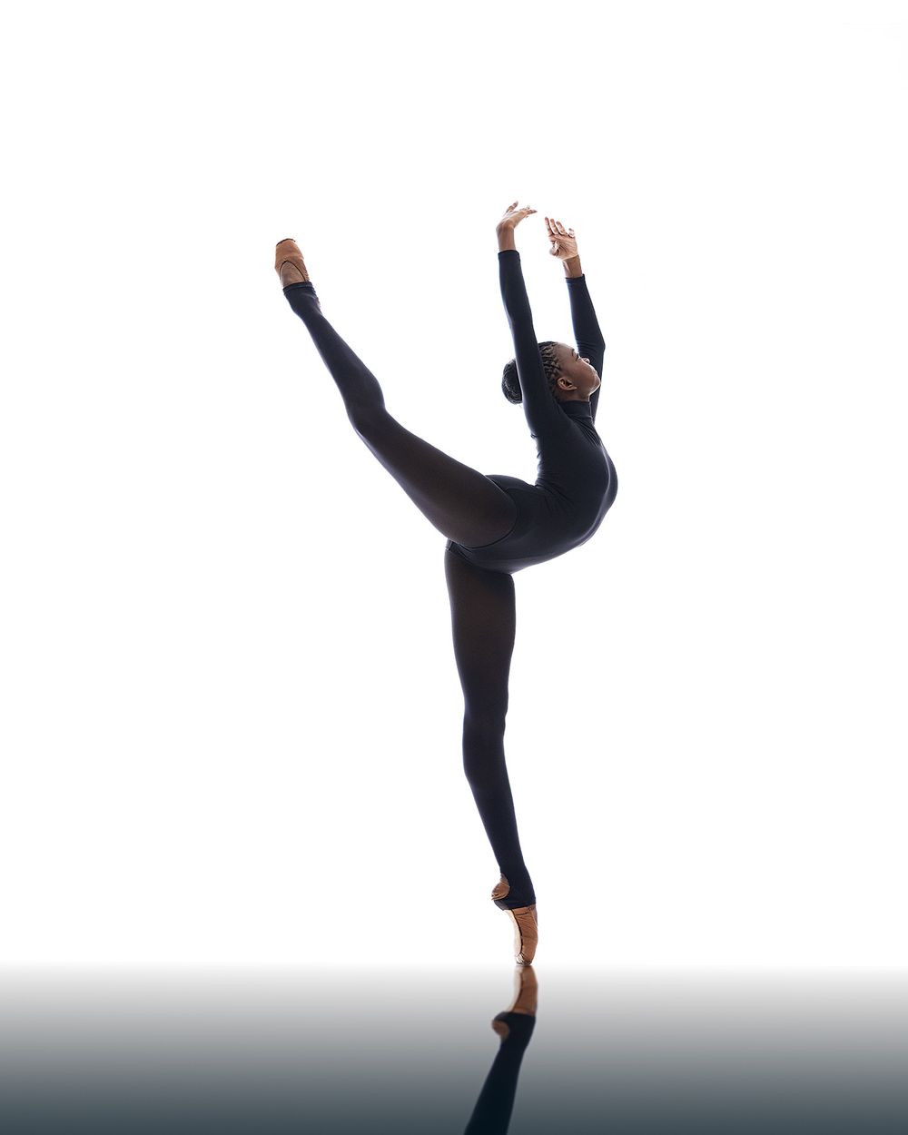 Contemporary dancer performing high kick movement in dramatic silhouette against gray background.