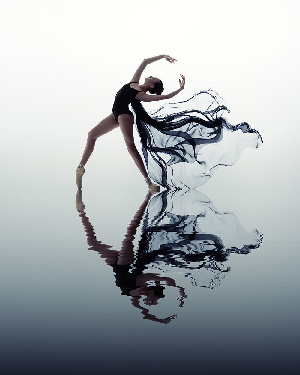A fluid black ink droplet creates an abstract reflection pattern against a light gray background in a minimalist composition.