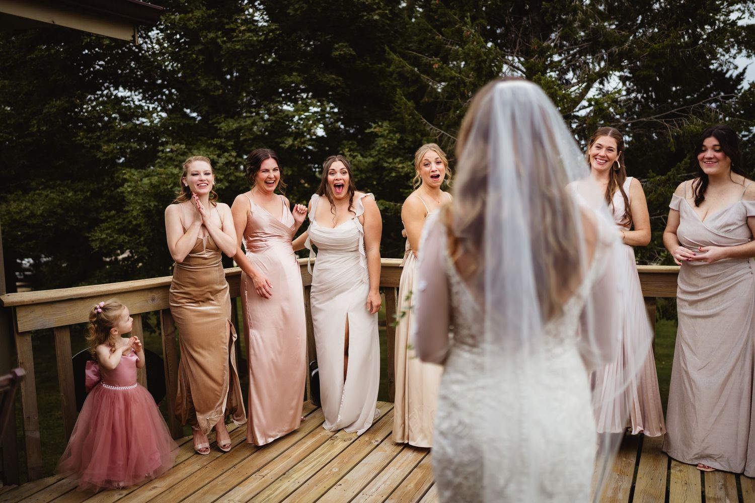 Wedding party members in neutral and blush toned dresses standing together and laughing during outdoor celebration.