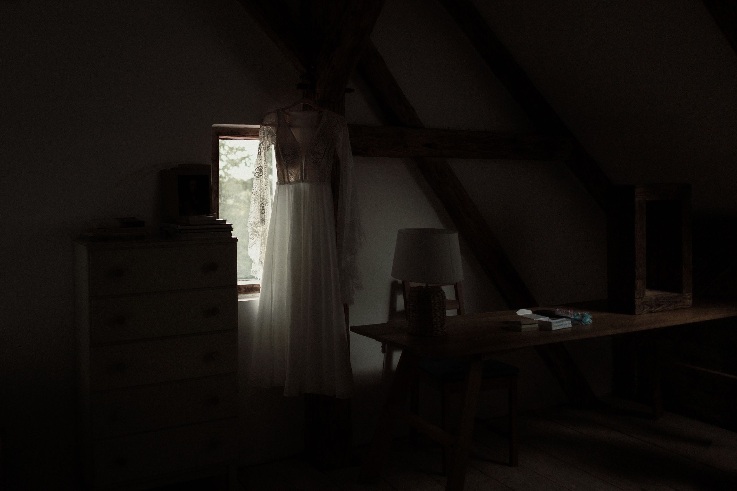 Dark attic room interior with sunlight streaming through doorway illuminating shadowy wooden furniture and rafters.