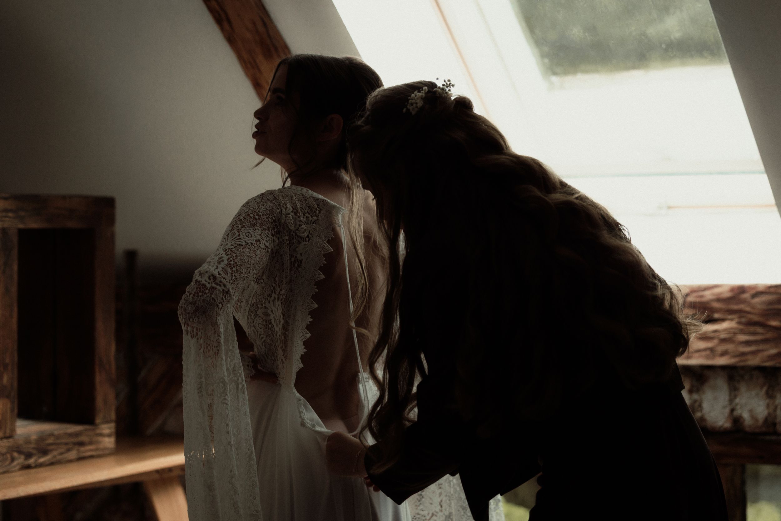 Silhouette of people in an attic room with slanted window, preparing for a special occasion in moody lighting.