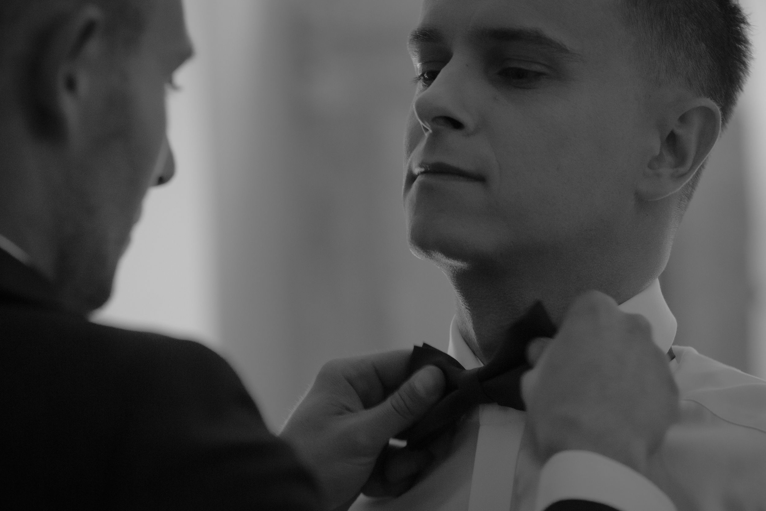 Black and white photo of someone adjusting another person's formal bowtie before an event.