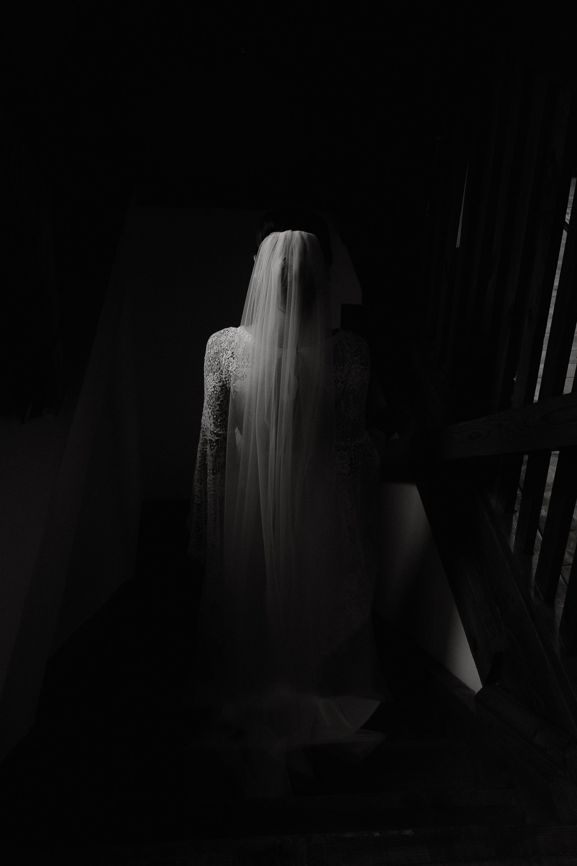 A ghostly white figure draped in fabric emerges from the darkness in a dramatic black and white photograph.