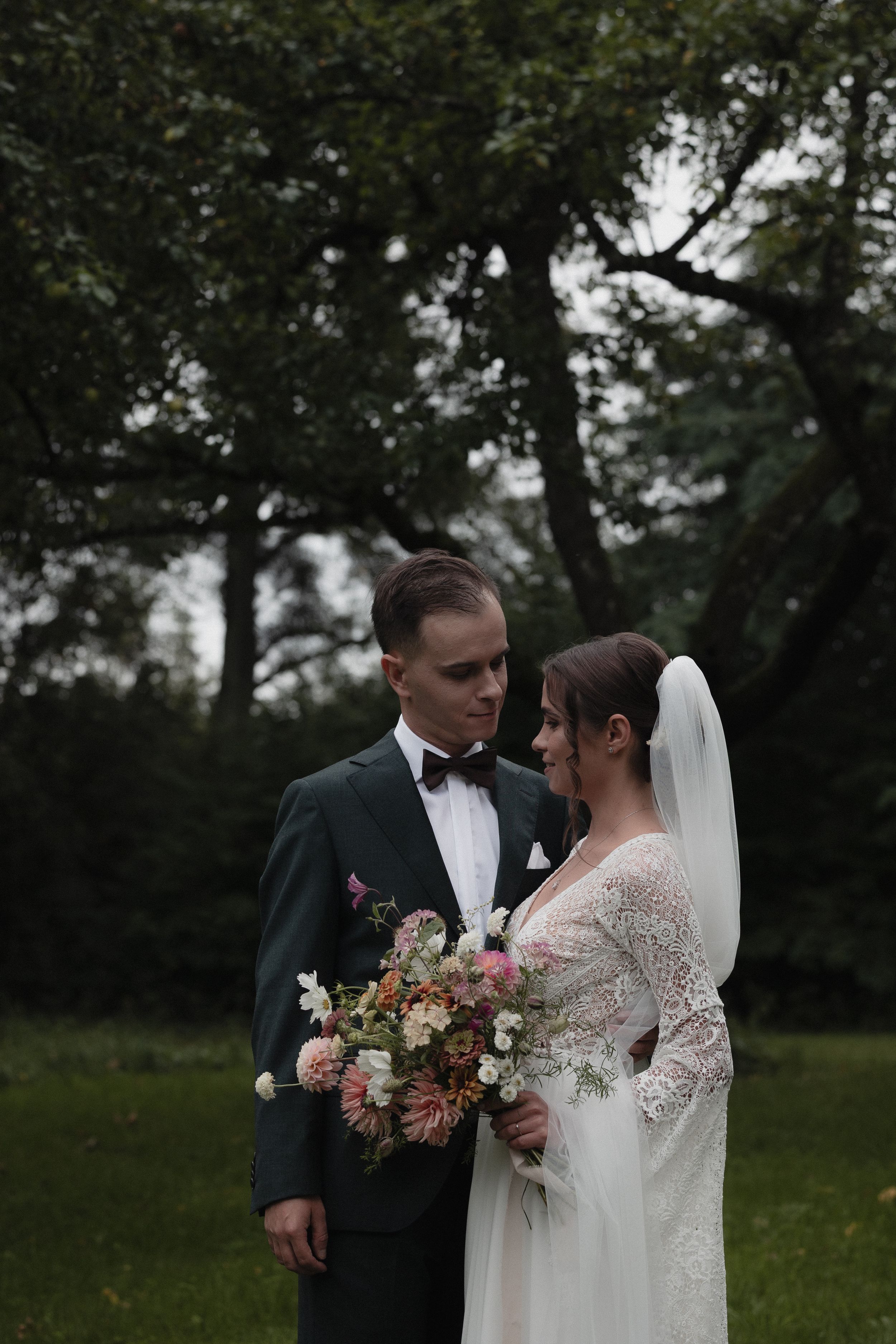 Bride and groom share intimate moments in a romantic outdoor wedding setting with lush greenery and floral bouquets.