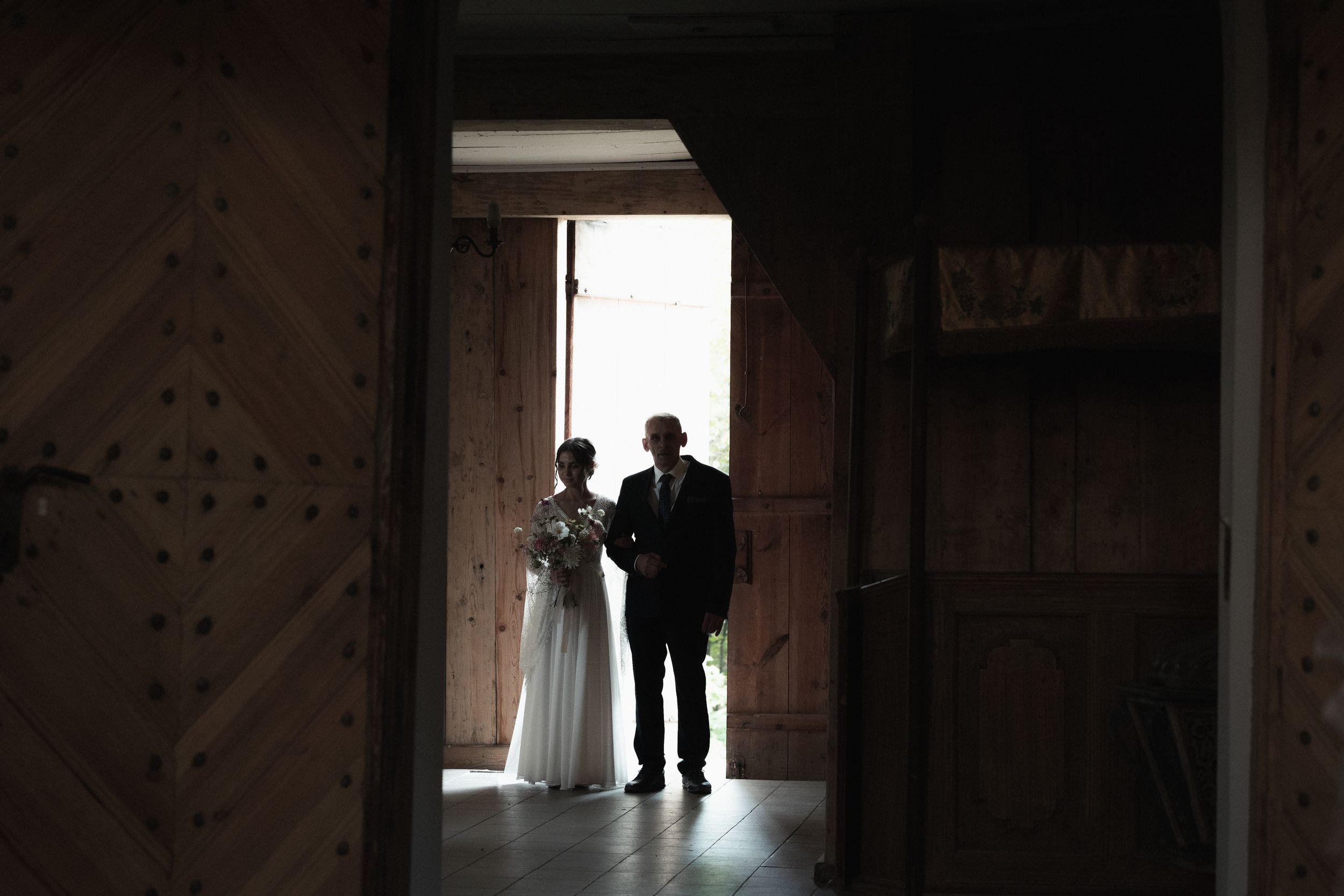 A silhouetted couple stands in a doorway of a rustic wooden building with dramatic backlighting.