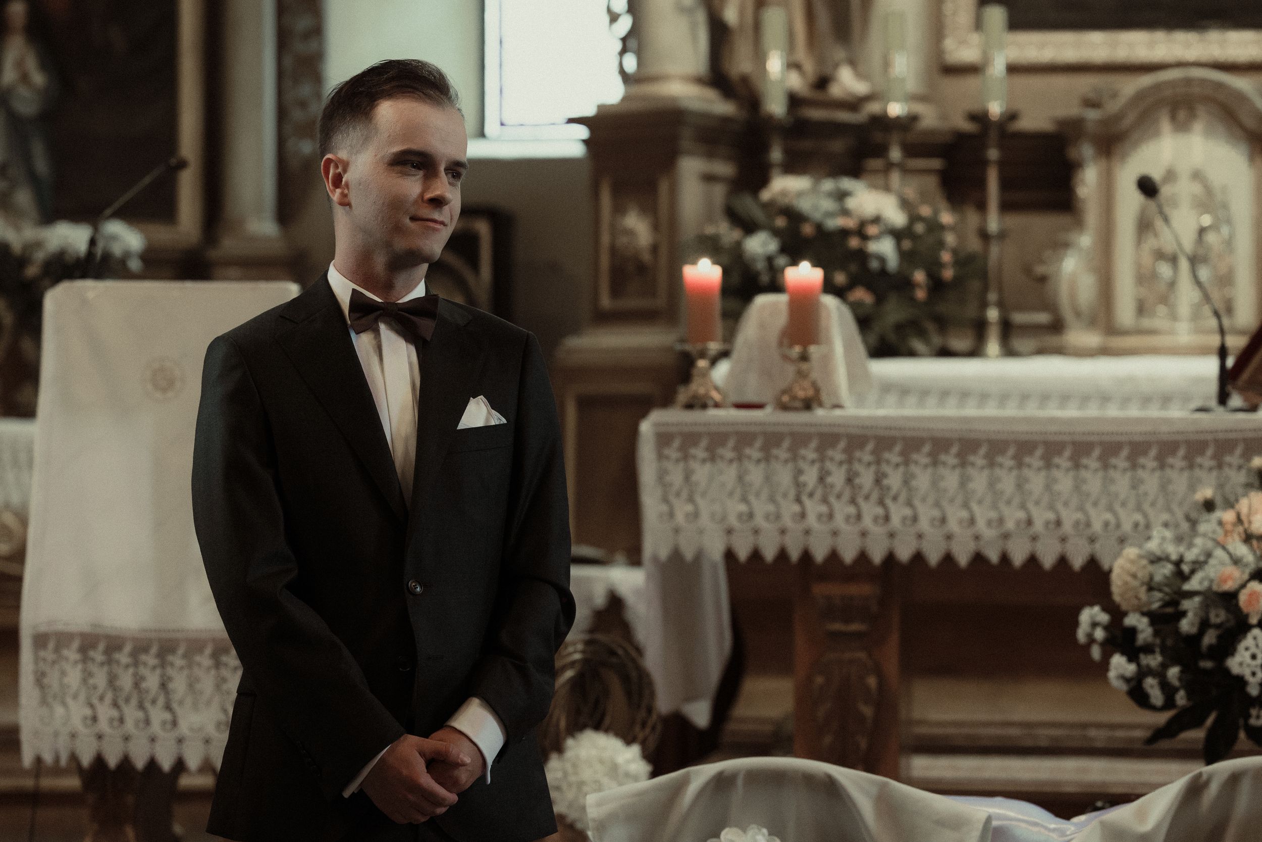 Groom waits anxiously at elegant church altar with ornate decor and glowing candles in background.