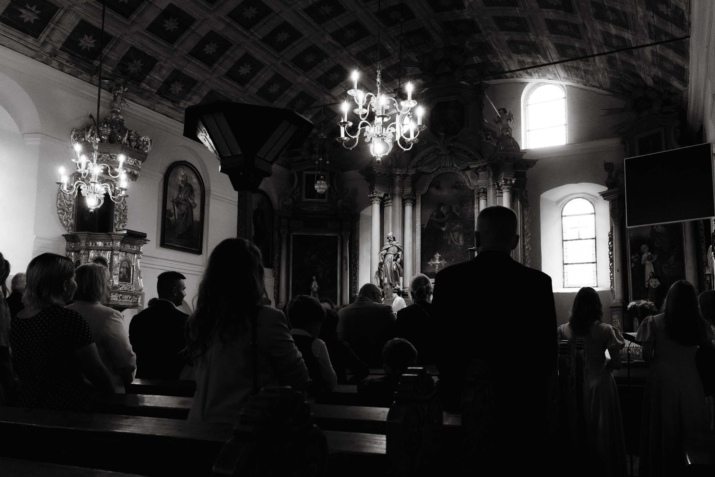 Dark interior of church with chandeliers and silhouettes during ceremony.