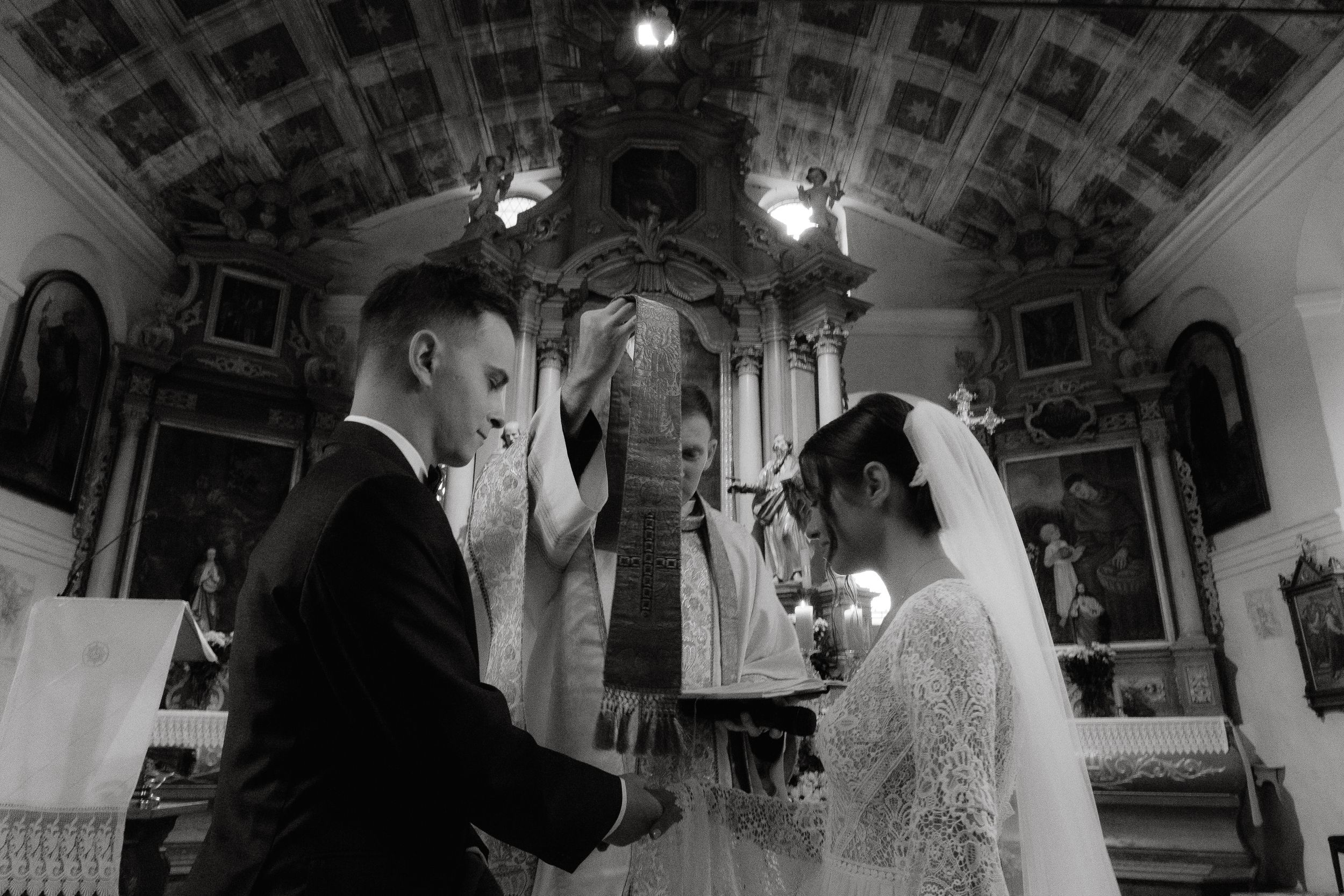 A wedding ceremony moment captured in an elegant church sanctuary with dramatic overhead lighting and architectural details.